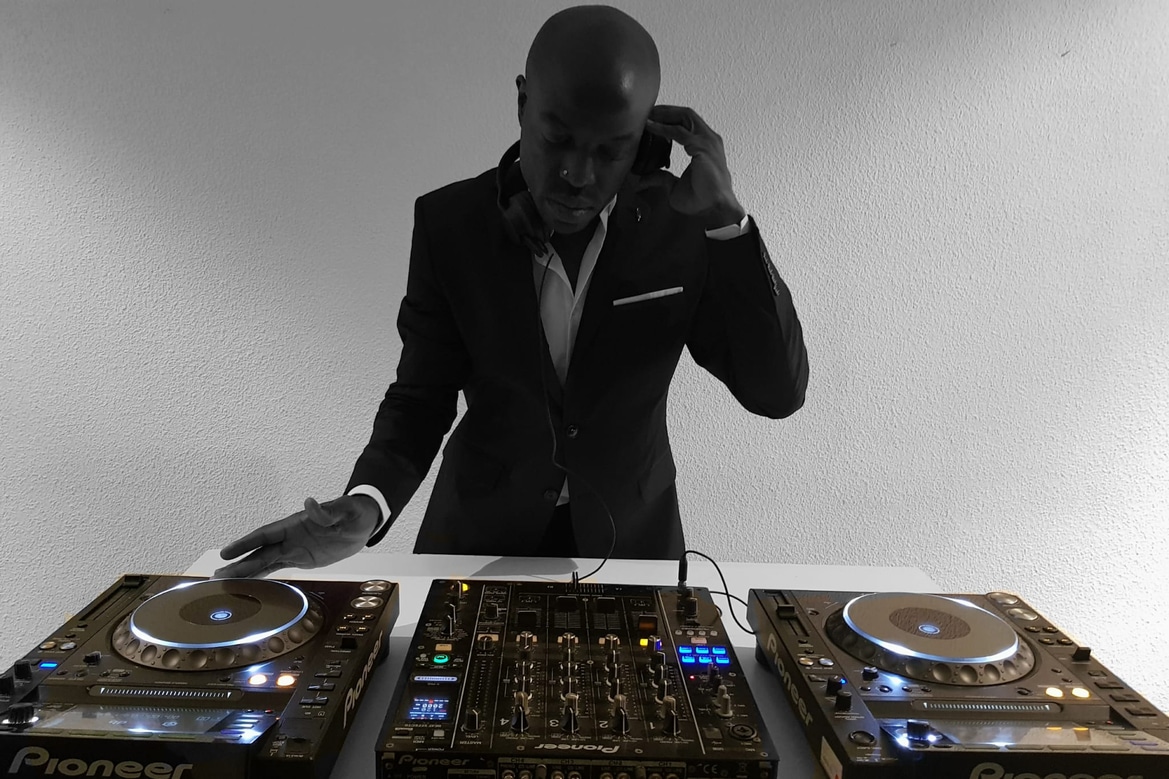 Foto en blanco y negro de un DJ de traje sosteniendo sus audífonos sobre la cabina