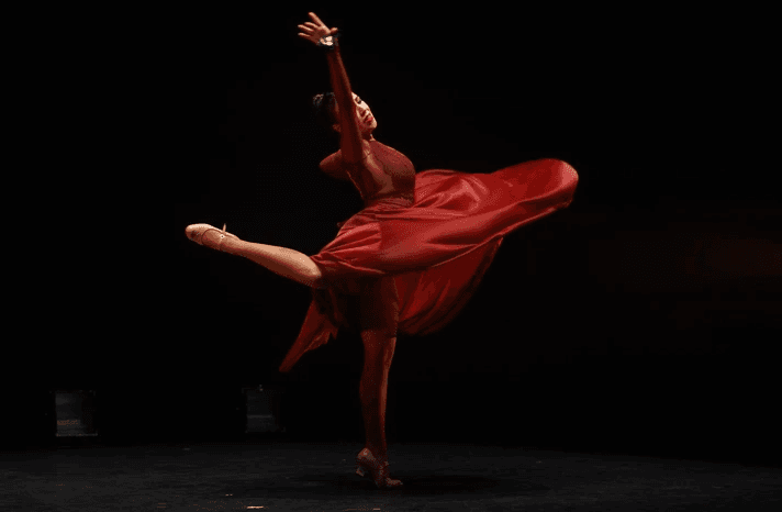 Bailarina con vestido rojo girando en un escenario oscuro