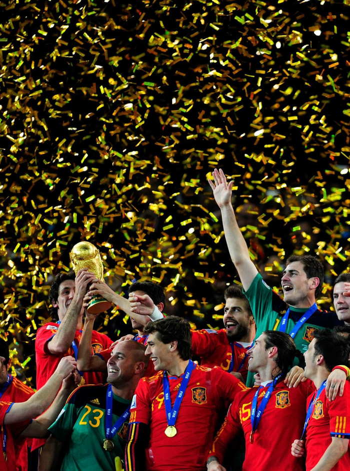 Futbolistas con camiseta roja levantando un trofeo dorado entre confeti