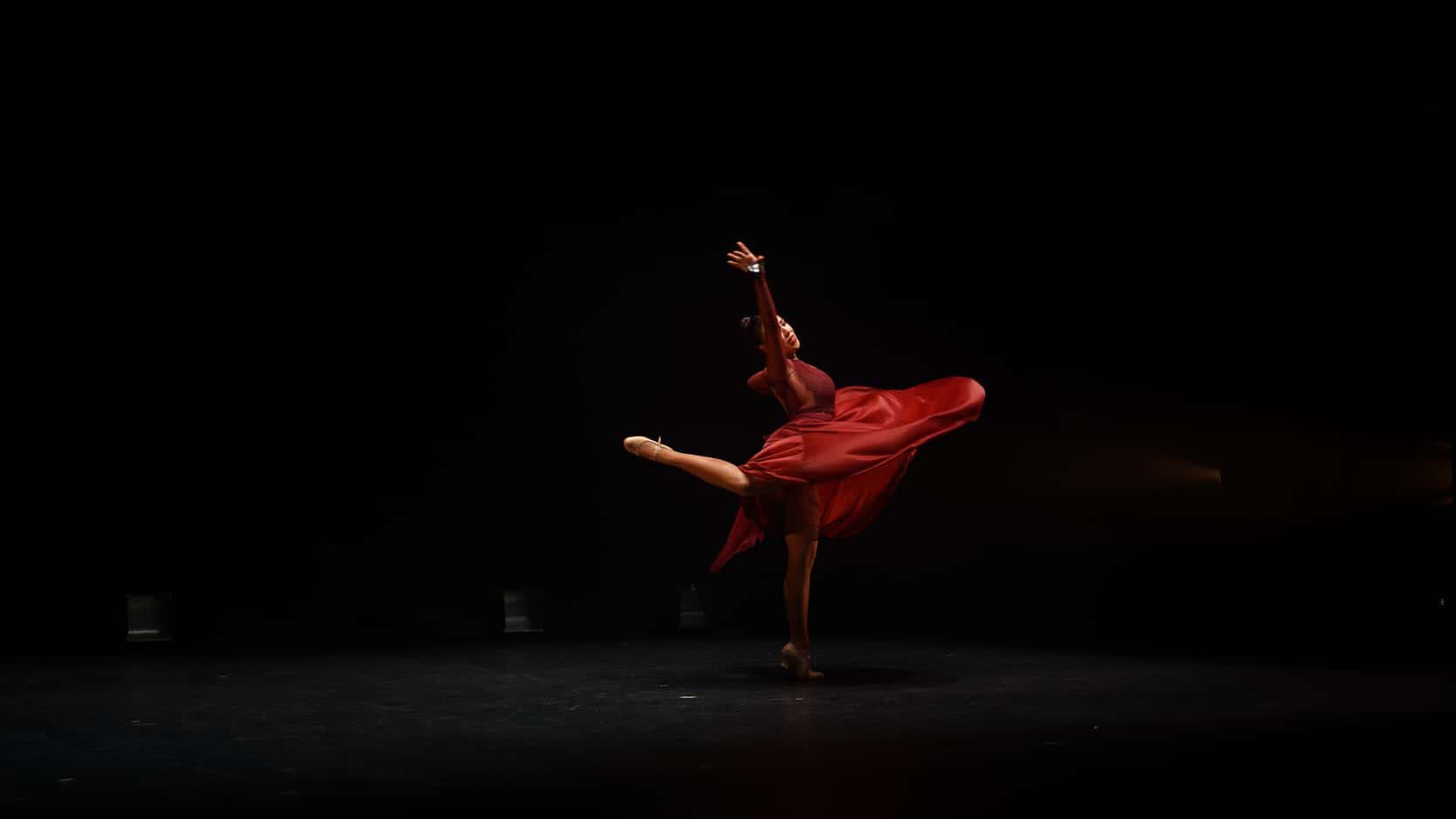 Bailarina con vestido rojo girando en un escenario oscuro