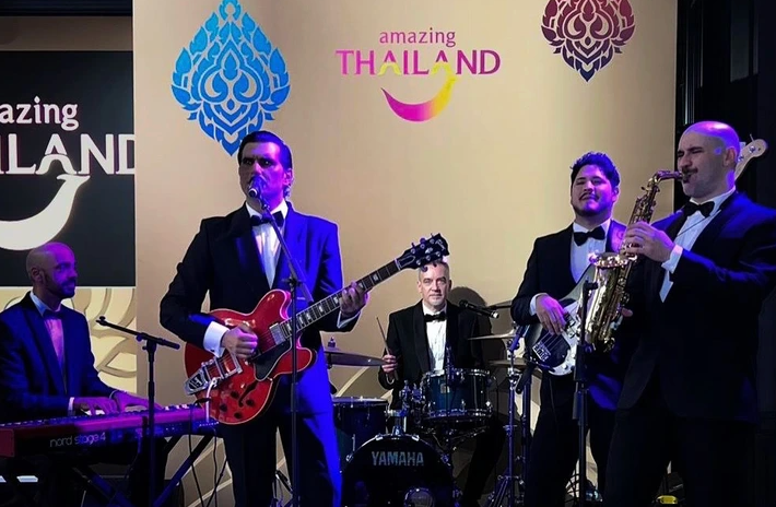 Banda de esmoquin tocando frente a un fondo con el lema «Amazing Thailand»