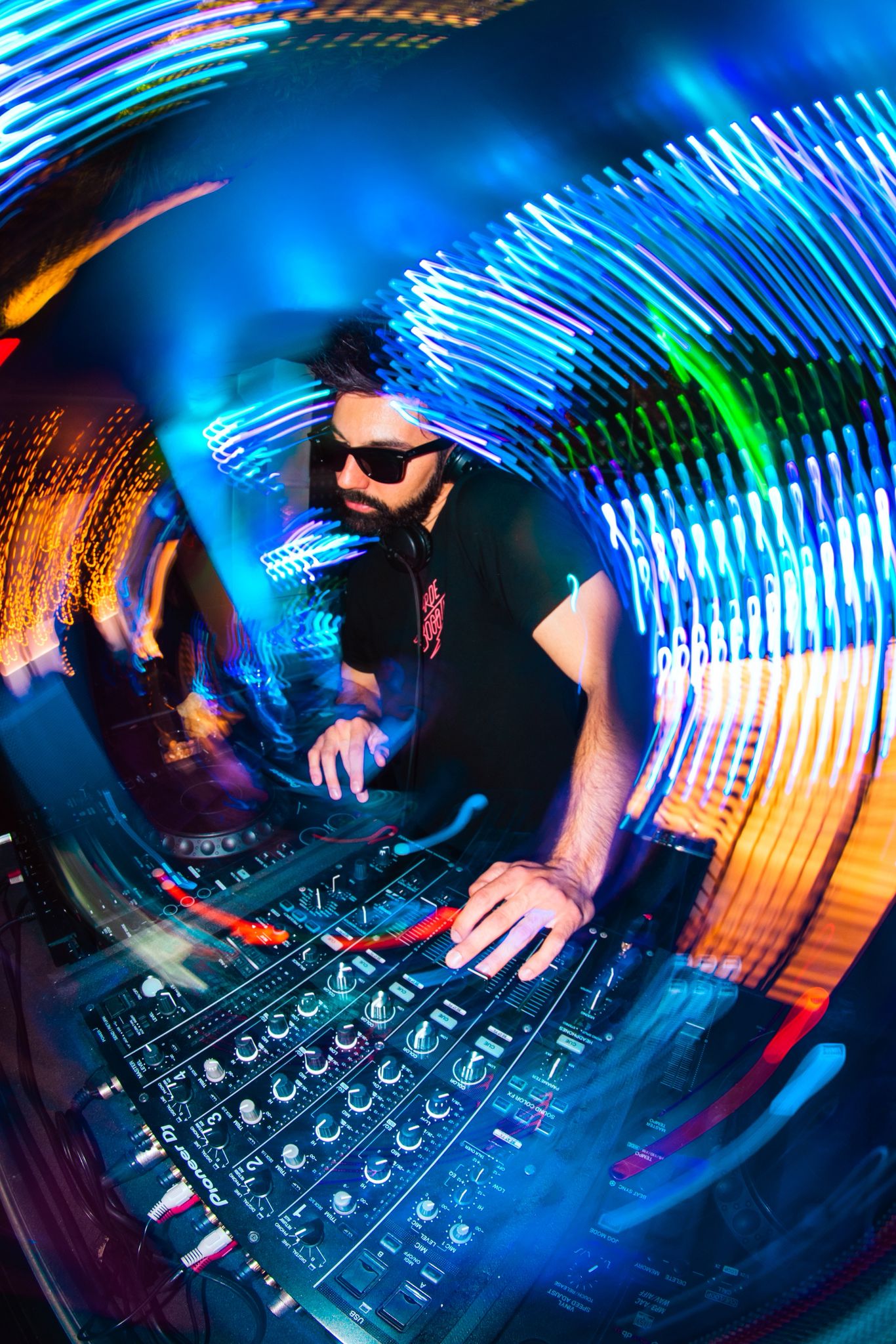 DJ con lentes oscuros en la mezcladora, rodeado de estelas de luz de colores