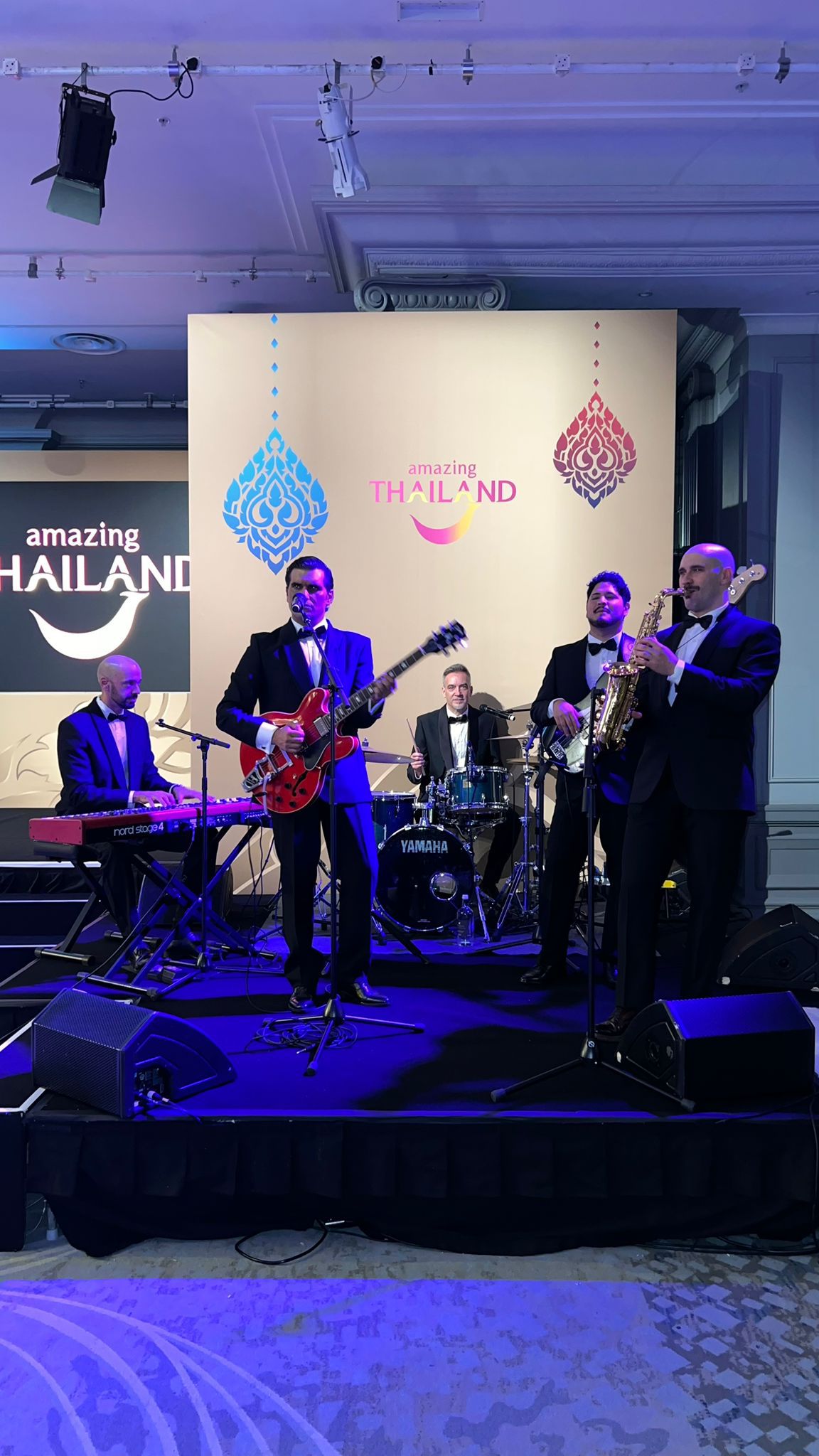 Banda de esmoquin tocando frente a un fondo con el lema «Amazing Thailand»